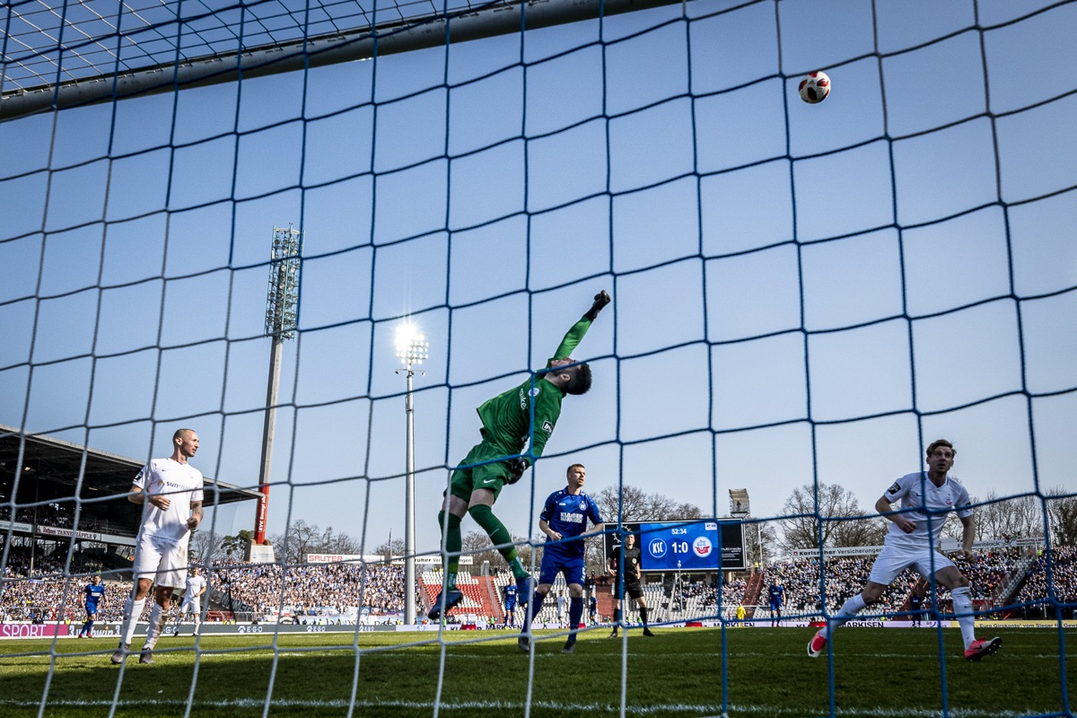 Blick durchs Tornetz auf Torwart und Spielfeld, Karlsruher SC gegen Hansa Rostock